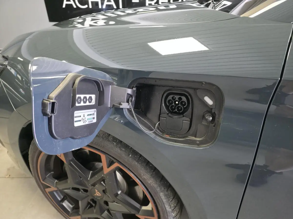 Prise de recharge ouverte côté arrière gauche sur CUPRA Leon bleu avec jante alliage 19'' cuivrée visible.