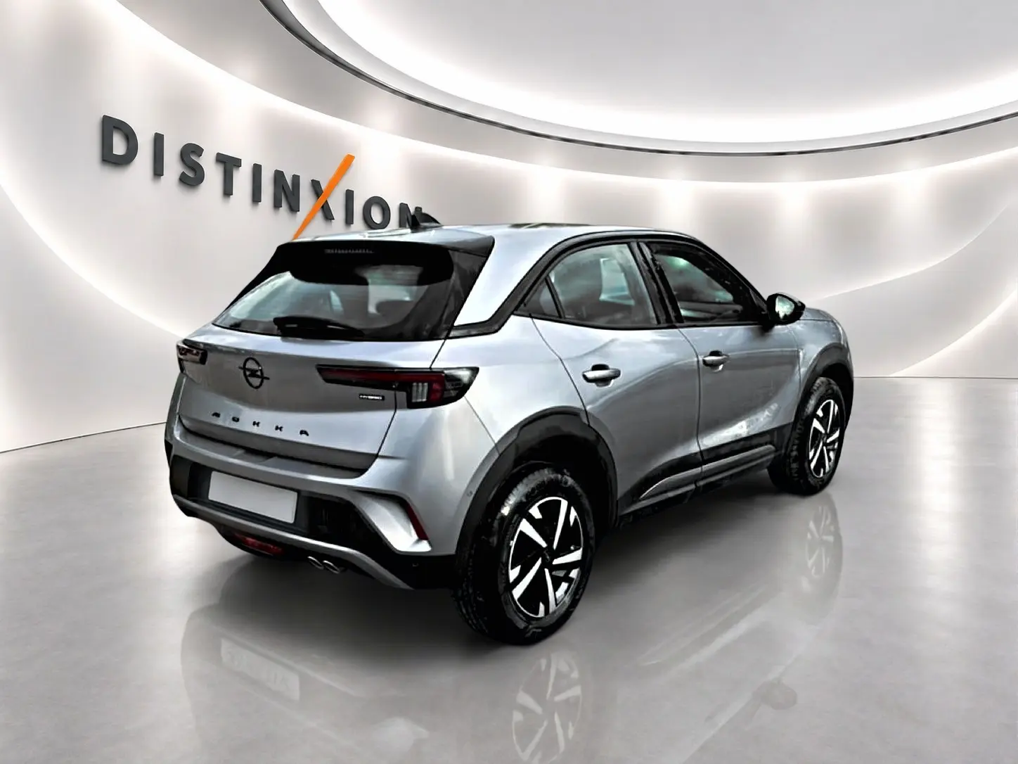 Vue 3/4 arrière droite d'un Opel Mokka gris 2025 avec feux arrière LED et jantes bicolores en studio lumineux.