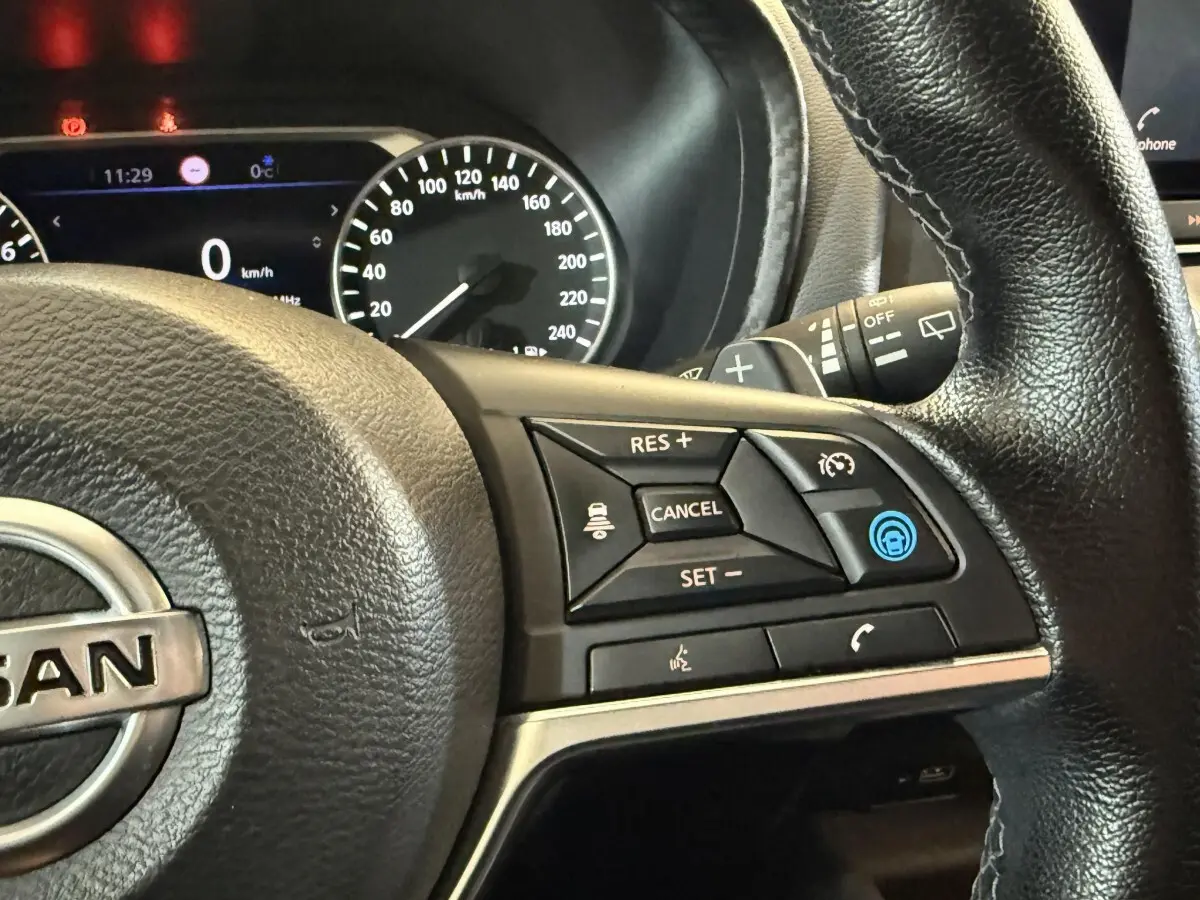 Gros plan sur le volant cuir noir du Nissan Juke 2021 avec commandes de régulateur et tableau de bord digital.