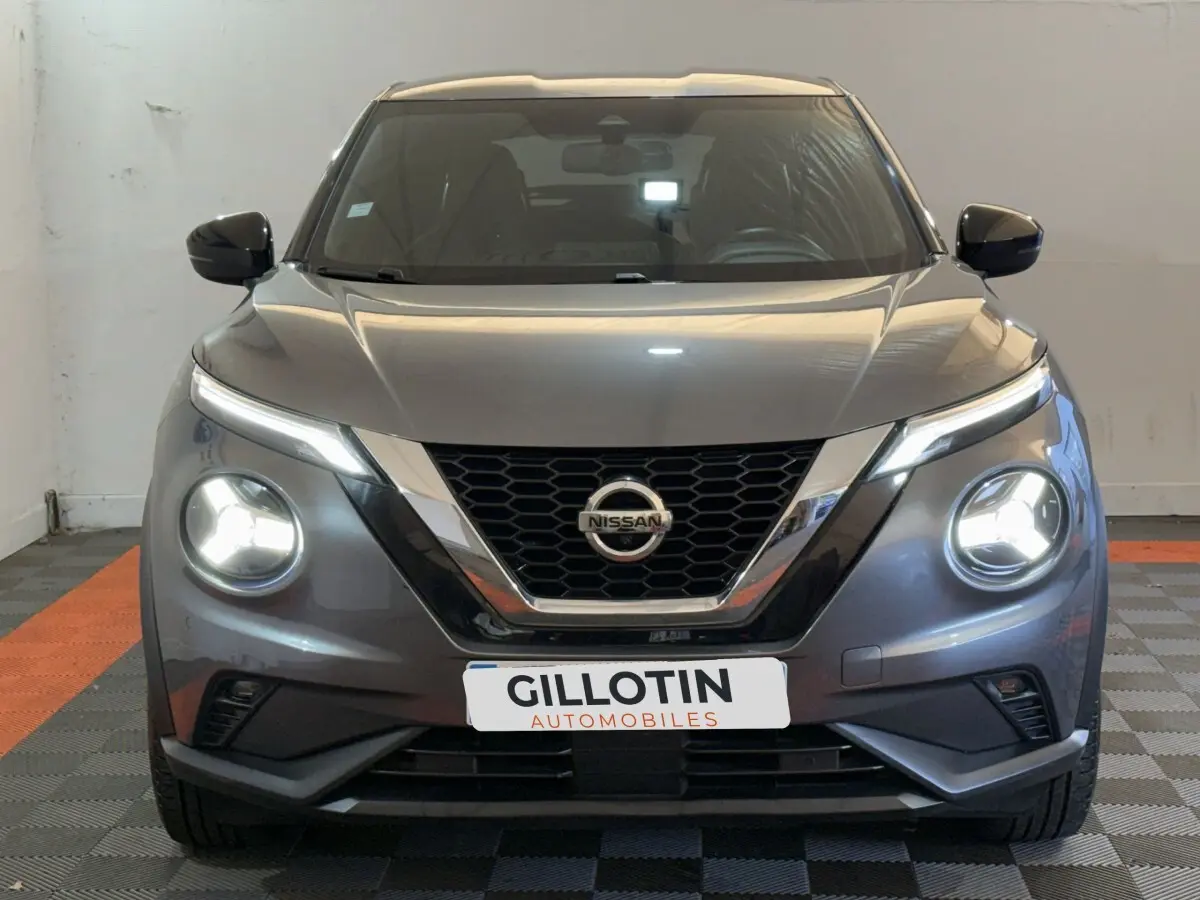 Vue frontale d'un Nissan Juke gris clair 2021 avec phares LED allumés dans un garage.