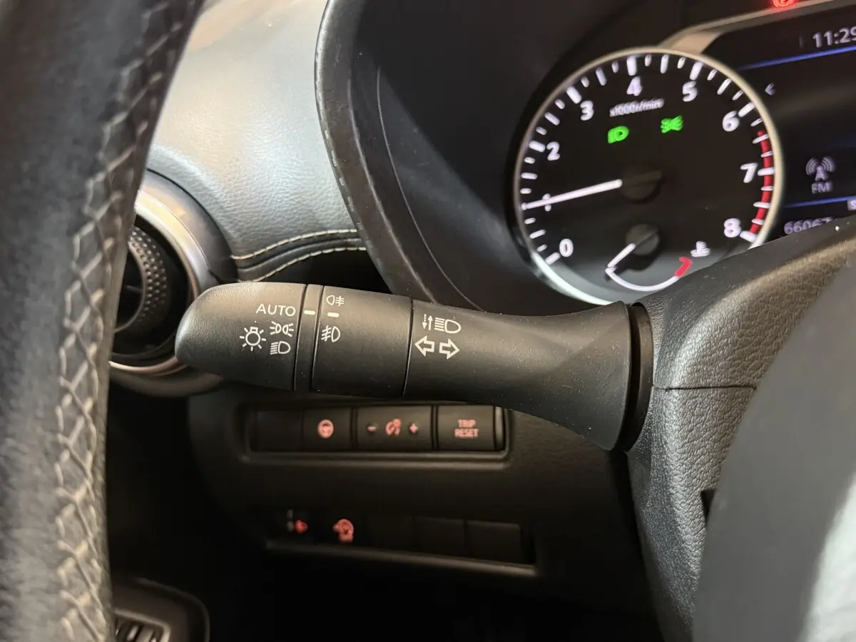 Gros plan sur la manette de phares et clignotants à gauche du volant dans le tableau de bord noir du Nissan Juke gris clair 2021.