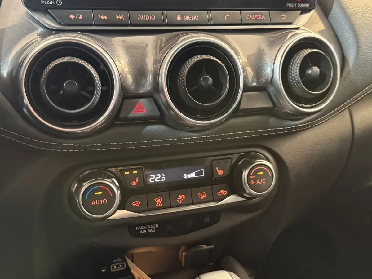 Détail du tableau de bord du Nissan Juke Tekna 2021 montrant les commandes de climatisation et les aérateurs ronds noirs.