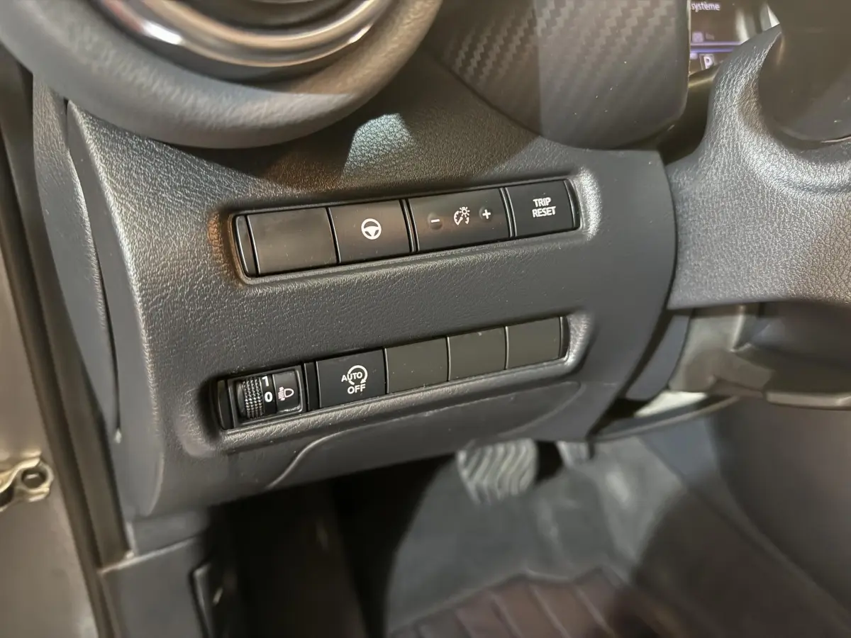 Gros plan sur les commandes côté gauche du tableau de bord gris du Nissan Juke Tekna 2021, avec réglages éclairage et régulateur.