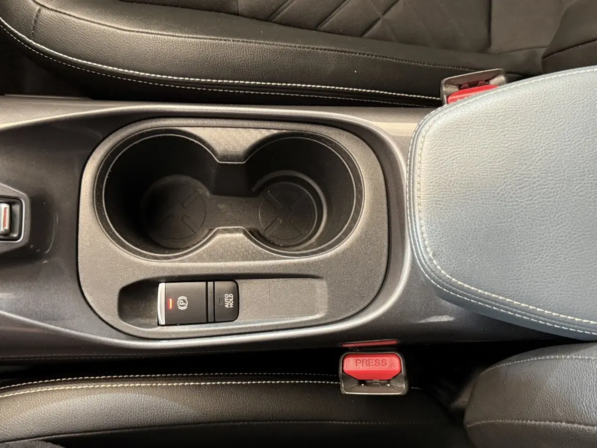 Gros plan sur la console centrale noire du Nissan Juke gris clair, avec porte-gobelets et frein à main électrique.