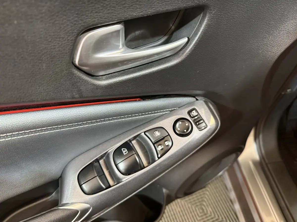 Gros plan sur la porte côté conducteur du Nissan Juke gris clair, montrant les commandes électriques et la poignée intérieure argentée.