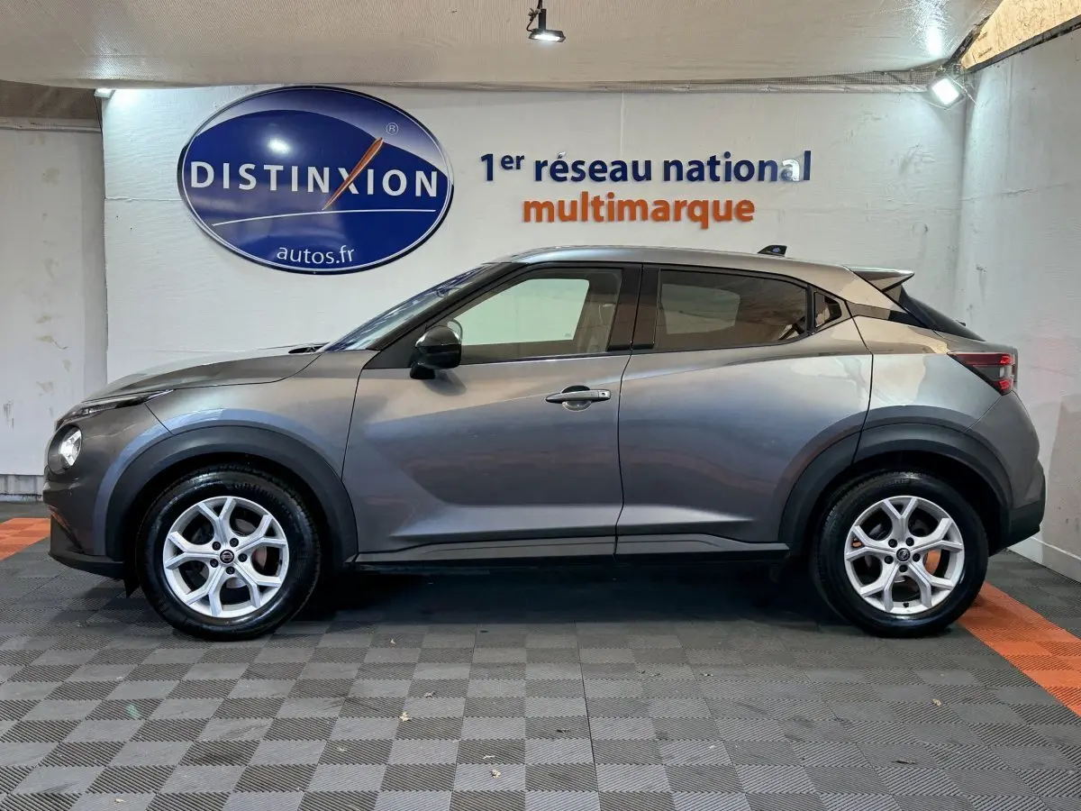Profil côté gauche d'un Nissan Juke gris clair 2021 avec jantes argentées, dans un showroom intérieur.