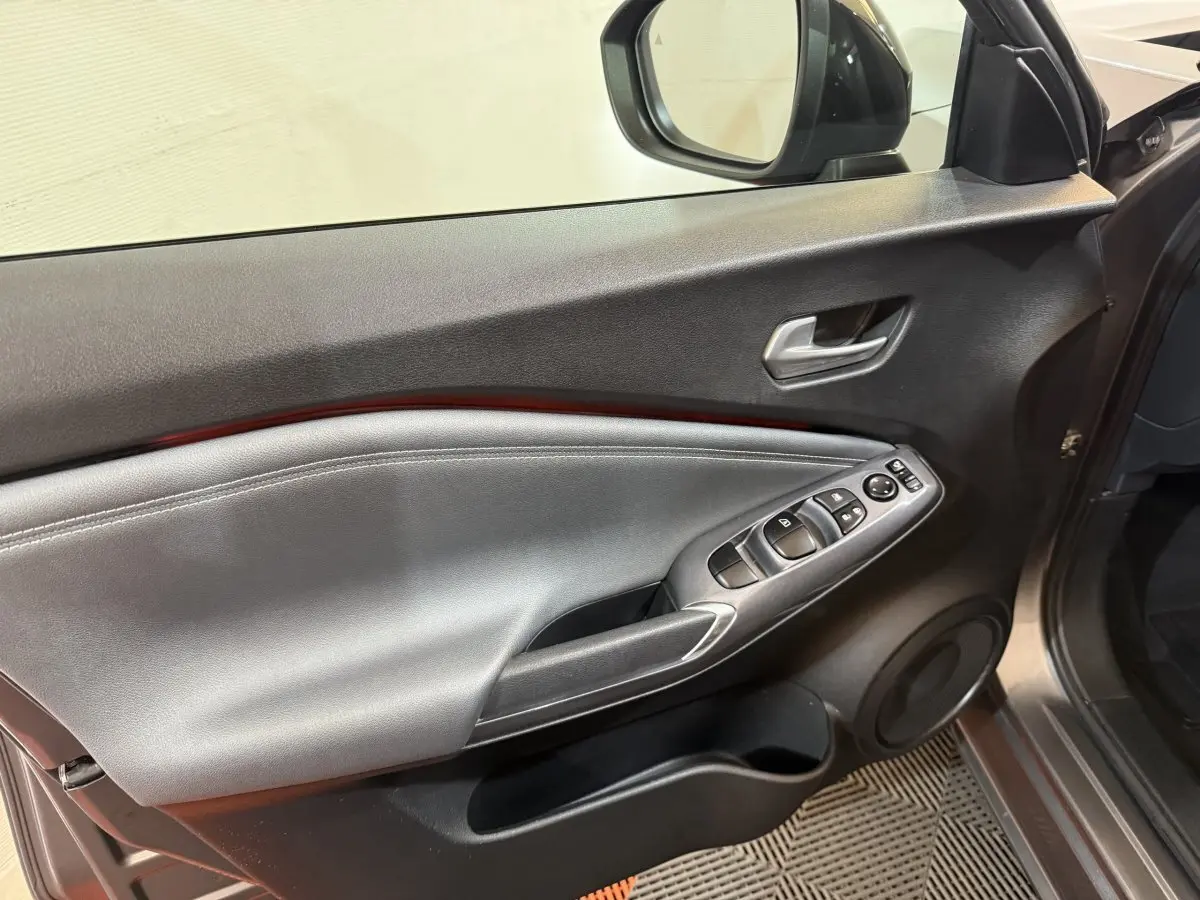 Vue intérieure du panneau de porte côté conducteur du Nissan Juke gris clair, avec commandes électriques et poignée argentée.