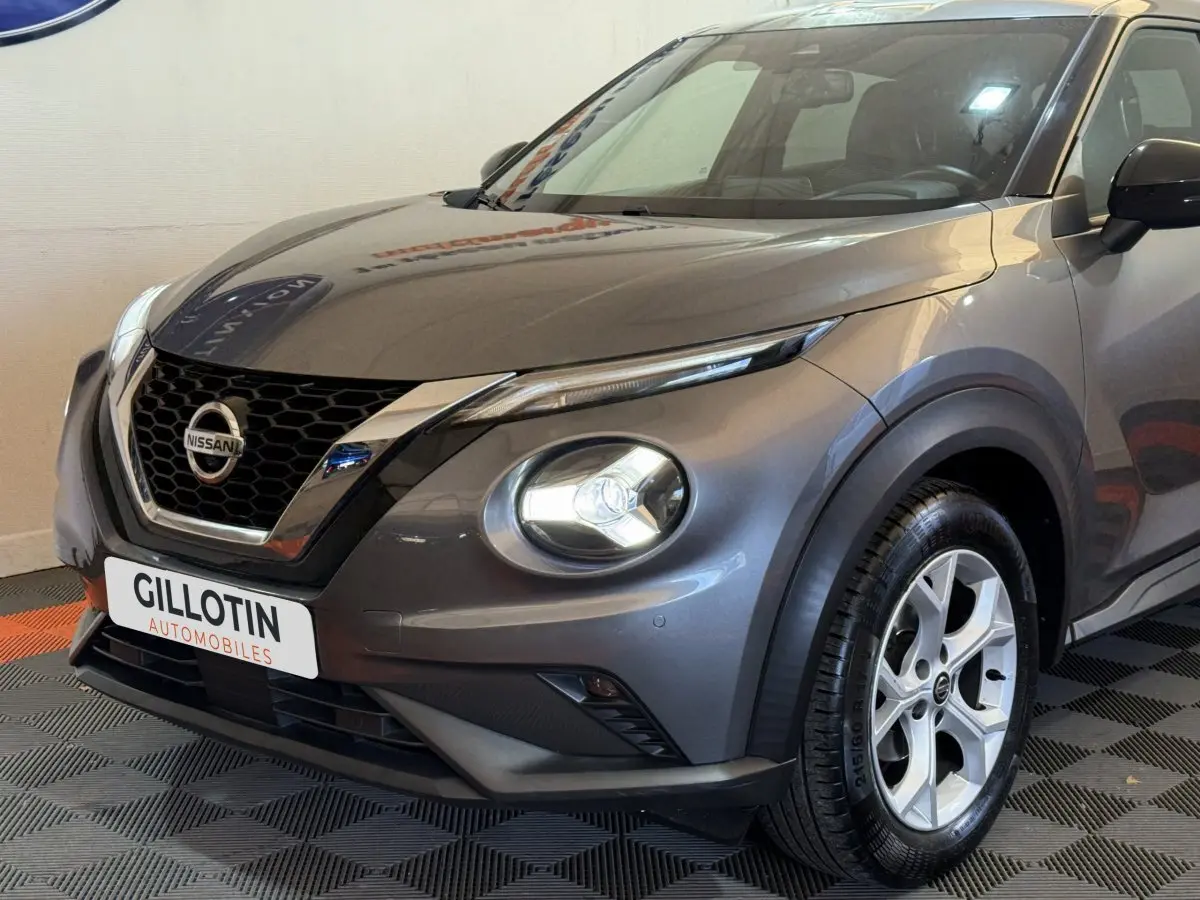 Vue 3/4 avant droit d'un Nissan Juke gris clair avec phares LED ronds et calandre en nid d'abeille chromée.