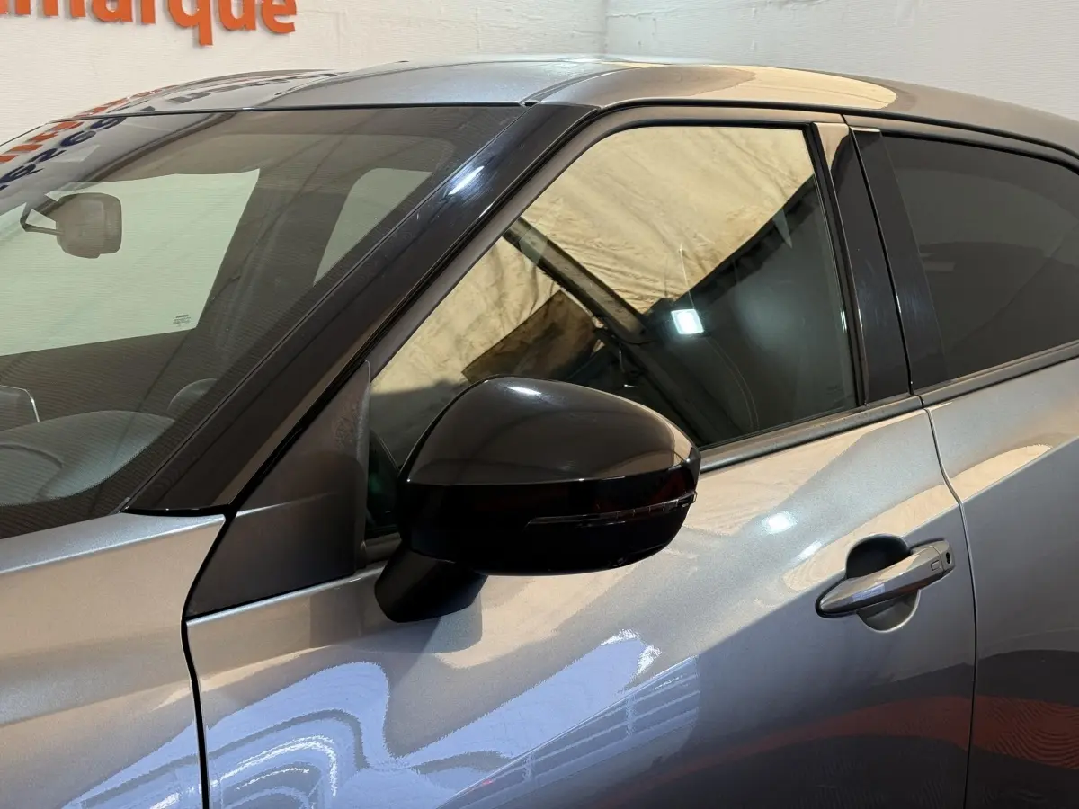 Vue côté gauche rapprochée du Nissan Juke gris clair 2021, mettant en valeur la portière et le rétroviseur noir brillant.