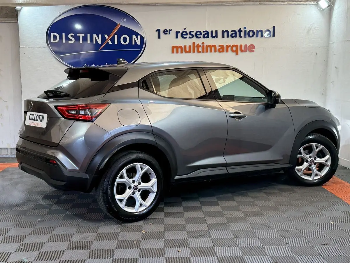Nissan Juke gris clair vu de profil côté gauche, avec jantes alliage et toit noir en arrière-plan showroom.