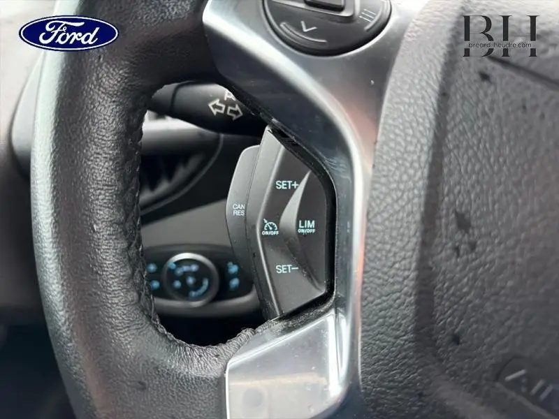 Gros plan sur les commandes du régulateur de vitesse sur le volant noir du Ford Transit Connect blanc glacier.