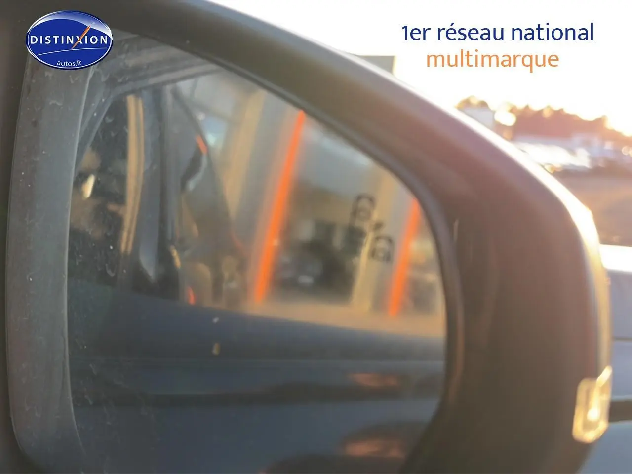 Rétroviseur extérieur droit d'un DS7 noir 2026, avec reflet flou de l'environnement urbain au coucher du soleil.