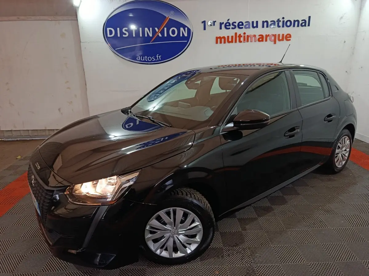 Peugeot 208 noire vue en 3/4 avant droit avec phares allumés, dans un showroom intérieur.