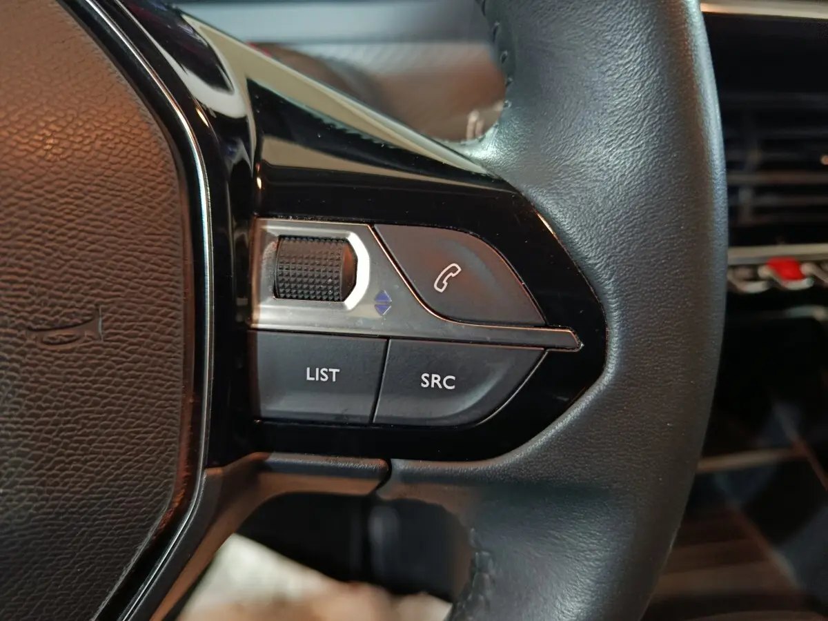 Gros plan sur les commandes gauche du volant noir de la Peugeot 208 1.2 PT 75 S&S Premium, boutons appel et liste.