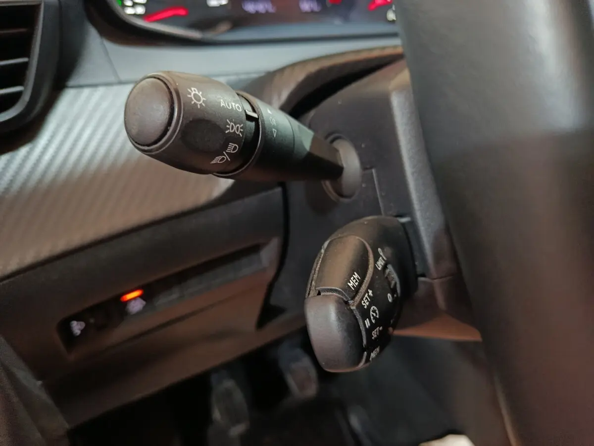 Gros plan sur les commandes de phares et régulateur de vitesse du tableau de bord noir du Peugeot 208 2022.