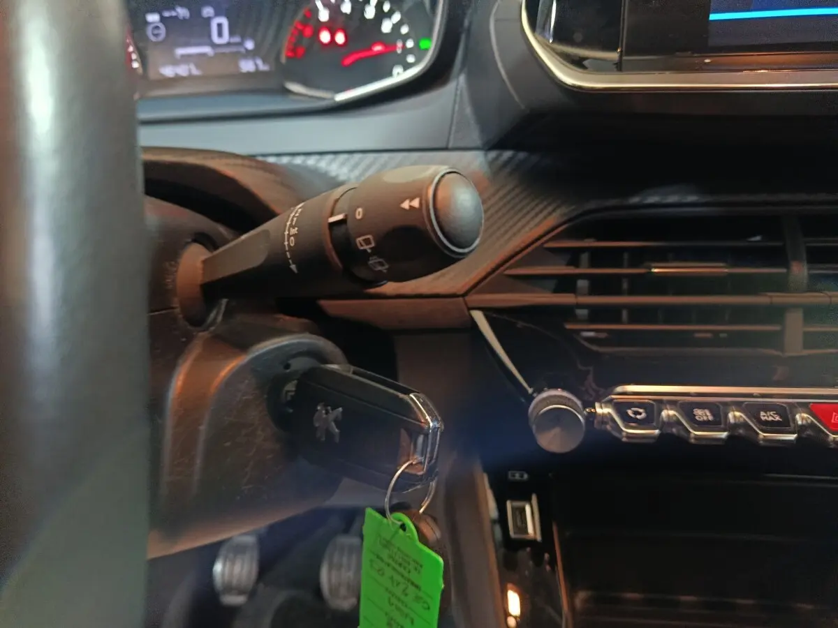 Vue intérieure du tableau de bord noir d'une Peugeot 208 2022, avec clé insérée et commandes centrales visibles.