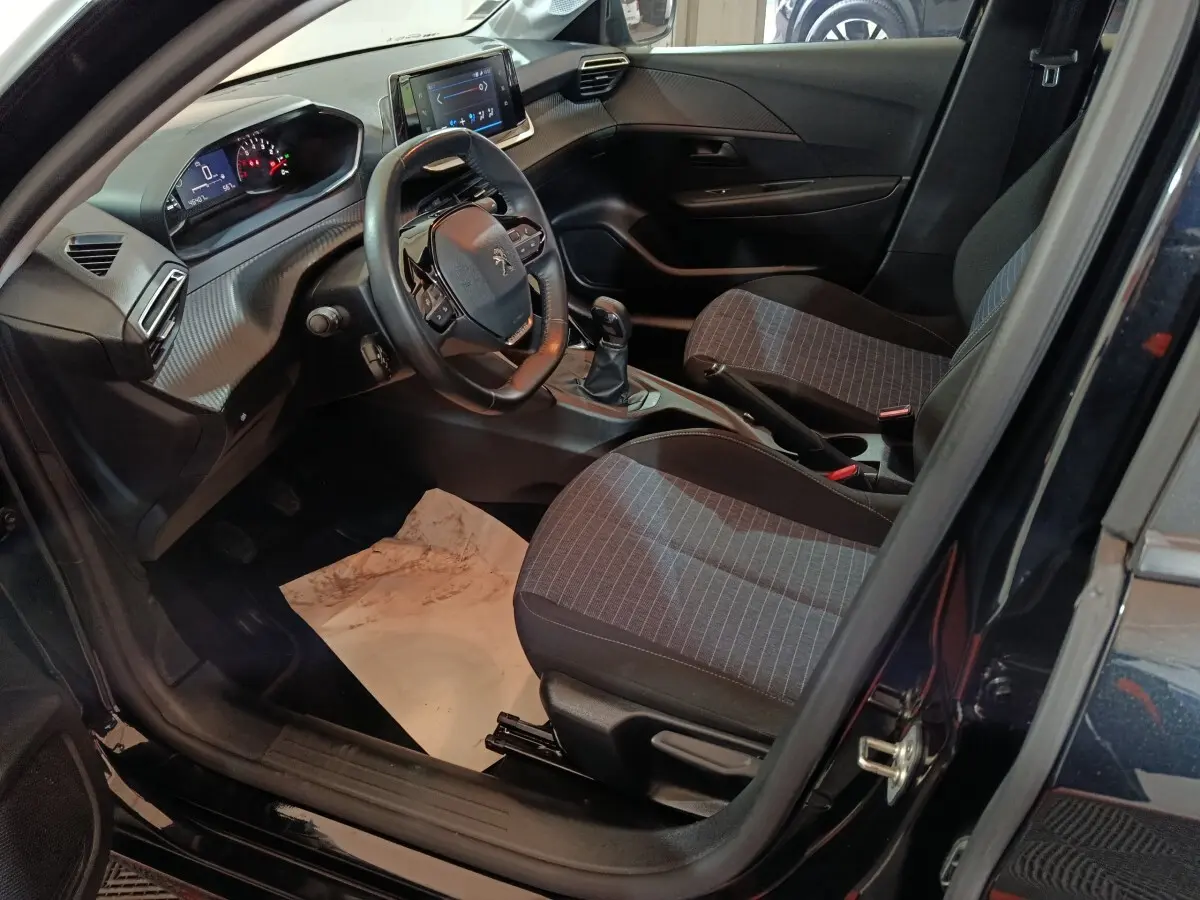 Intérieur avant droit de la Peugeot 208 noire 2022, volant compact, tableau de bord numérique et sièges tissu gris.
