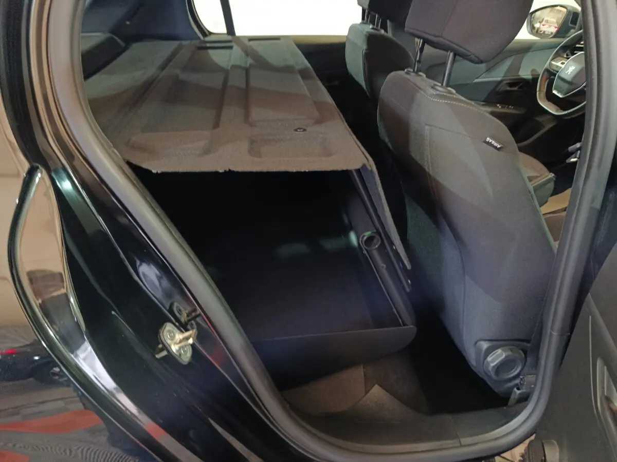 Vue intérieure côté gauche arrière d'une Peugeot 208 noire 2022 avec banquette arrière rabattue et coffre visible.