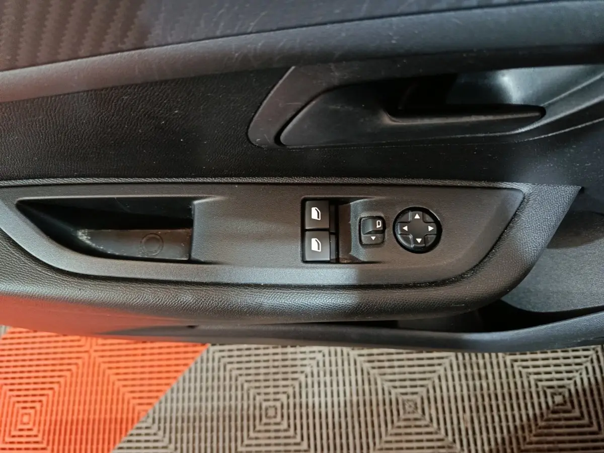 Vue rapprochée des commandes de réglage des rétroviseurs et des vitres côté conducteur d'une Peugeot 208 noire 2022.