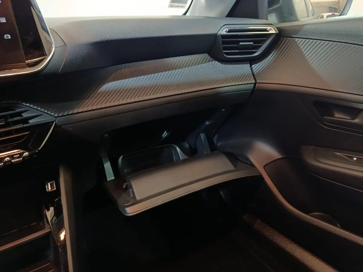 Intérieur côté passager de la Peugeot 208 2022 noire, avec boîte à gants ouverte et tableau de bord texturé.