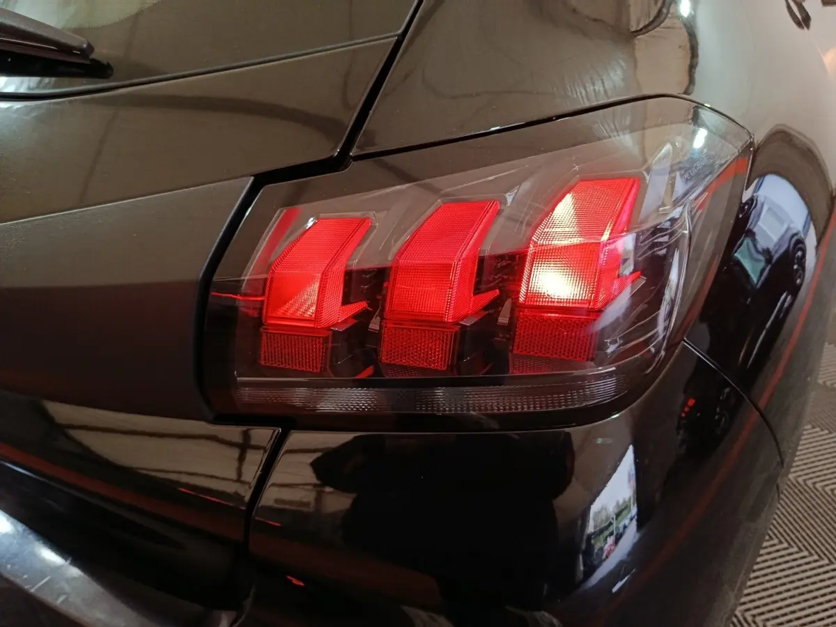 Gros plan sur le feu arrière droit rouge d'une Peugeot 208 noire, mettant en valeur ses trois griffes lumineuses distinctives.