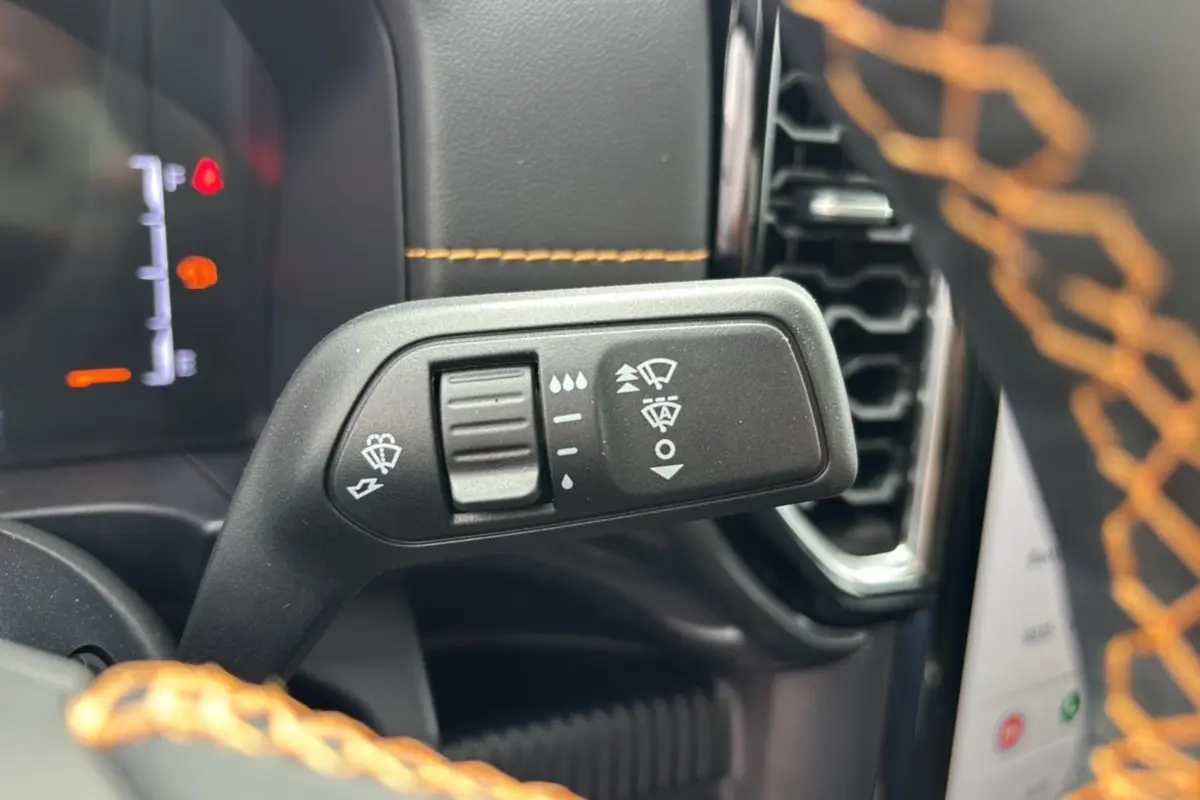 Gros plan sur la commande d’essuie-glace à gauche du volant avec surpiqûres orange du volant en cuir visible.