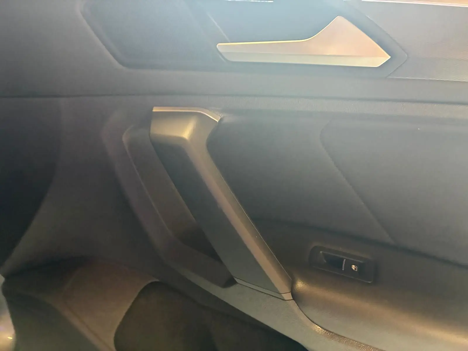 Détail de la porte intérieure côté droit du Volkswagen Tiguan gris, avec poignée angulaire et bouton de verrouillage.