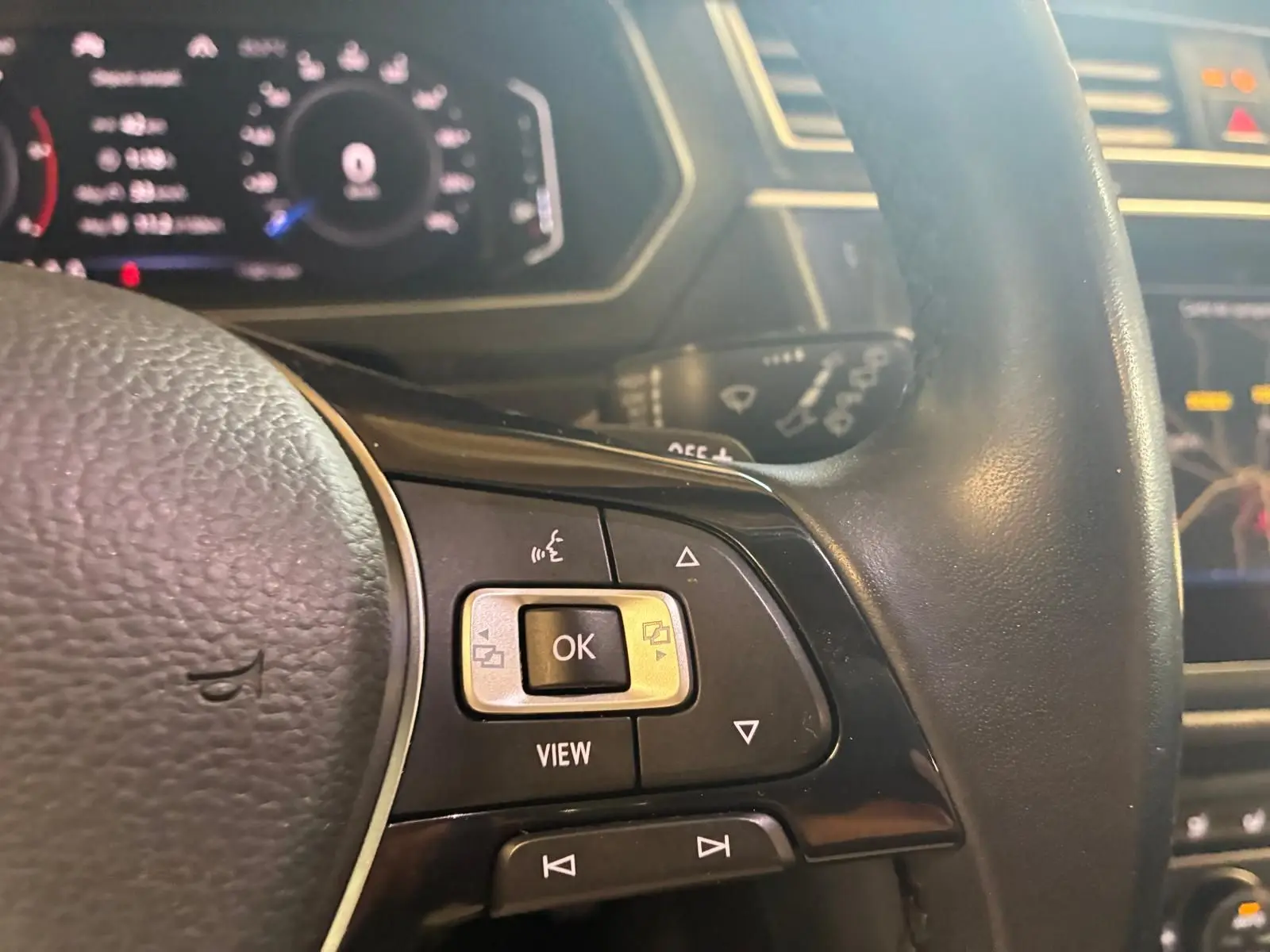 Gros plan sur les commandes du volant noir du Volkswagen Tiguan gris, avec tableau de bord numérique en arrière-plan.