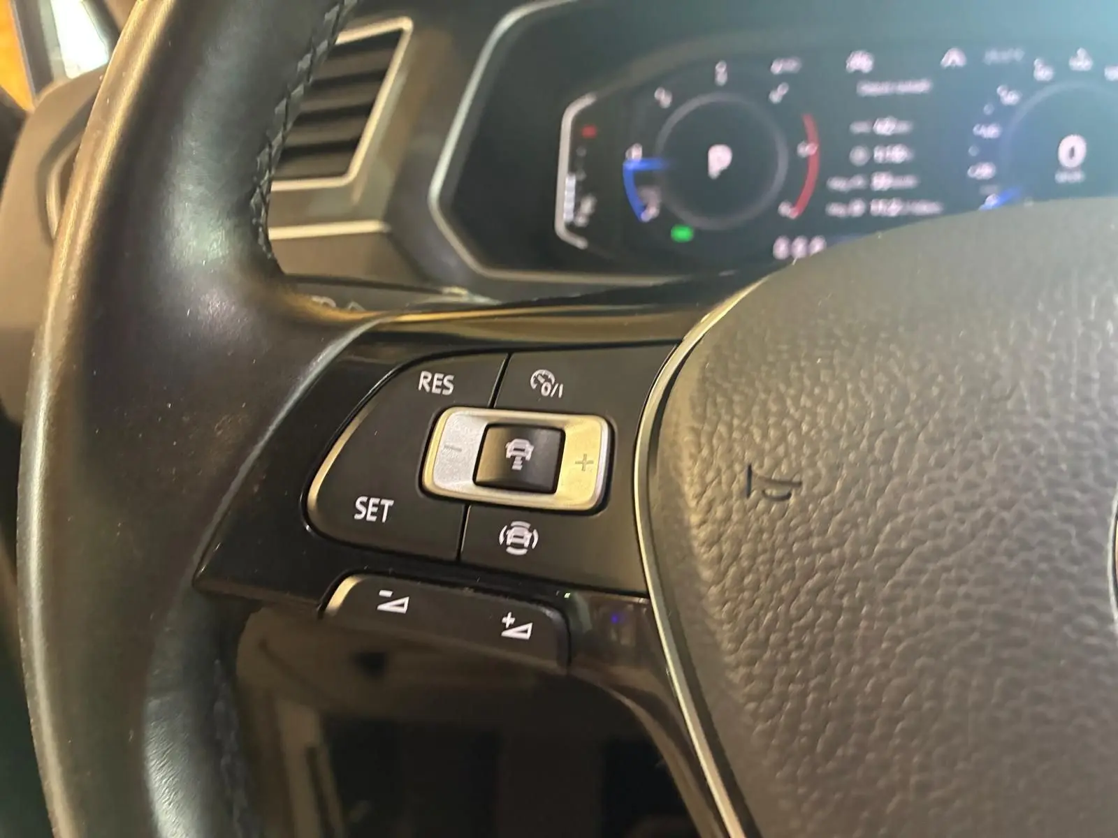 Gros plan sur le volant noir du Volkswagen Tiguan 2020 avec commandes de régulateur de vitesse et tableau de bord numérique flou.