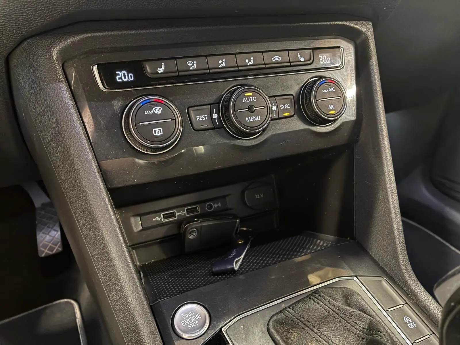 Vue rapprochée de la console centrale noire du Volkswagen Tiguan 2020, montrant les commandes de climatisation et le bouton start/stop.