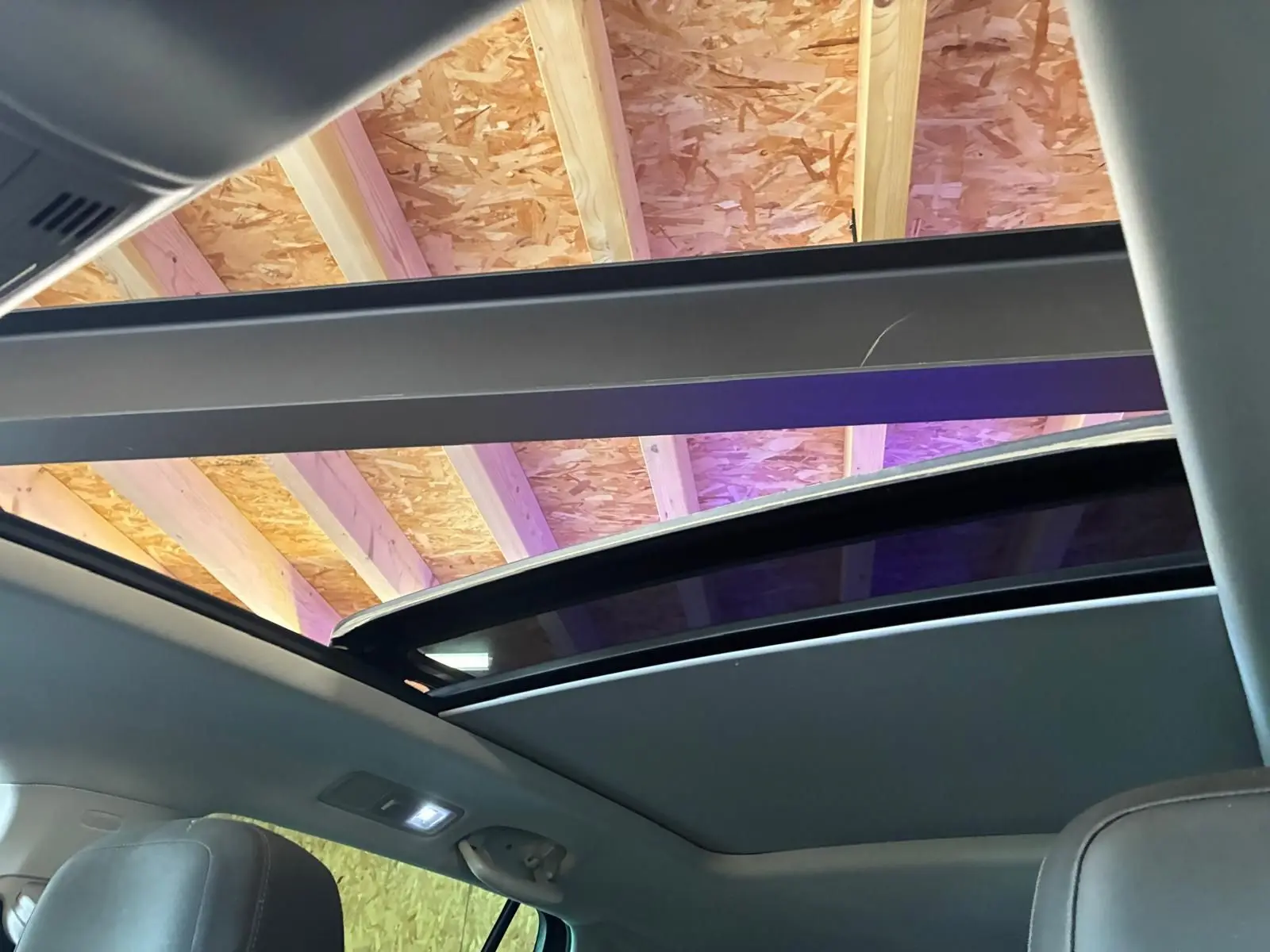 Vue intérieure du toit ouvrant panoramique ouvert du Volkswagen Tiguan gris, montrant la structure du plafond en bois.