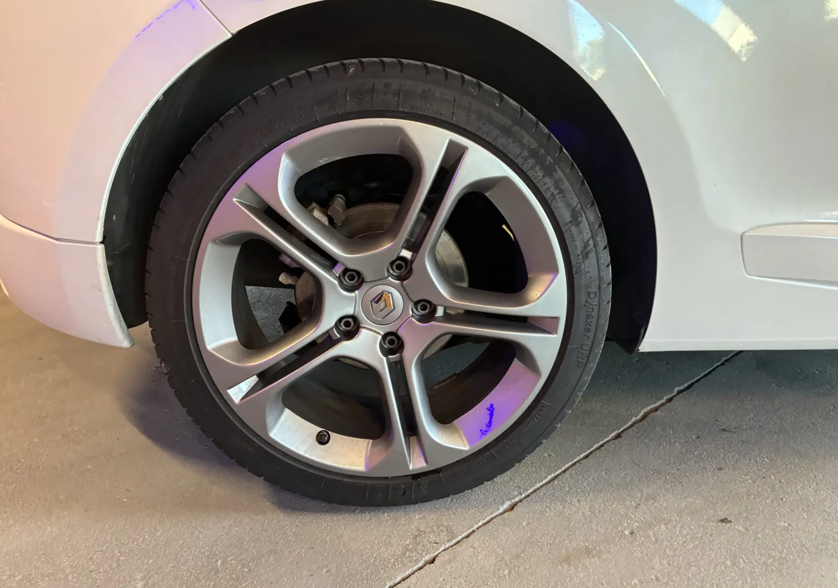 Gros plan sur la roue arrière droite blanche d’une Renault Mégane Coupé 2.0 DCI 165 GT avec jante alliage cinq branches.