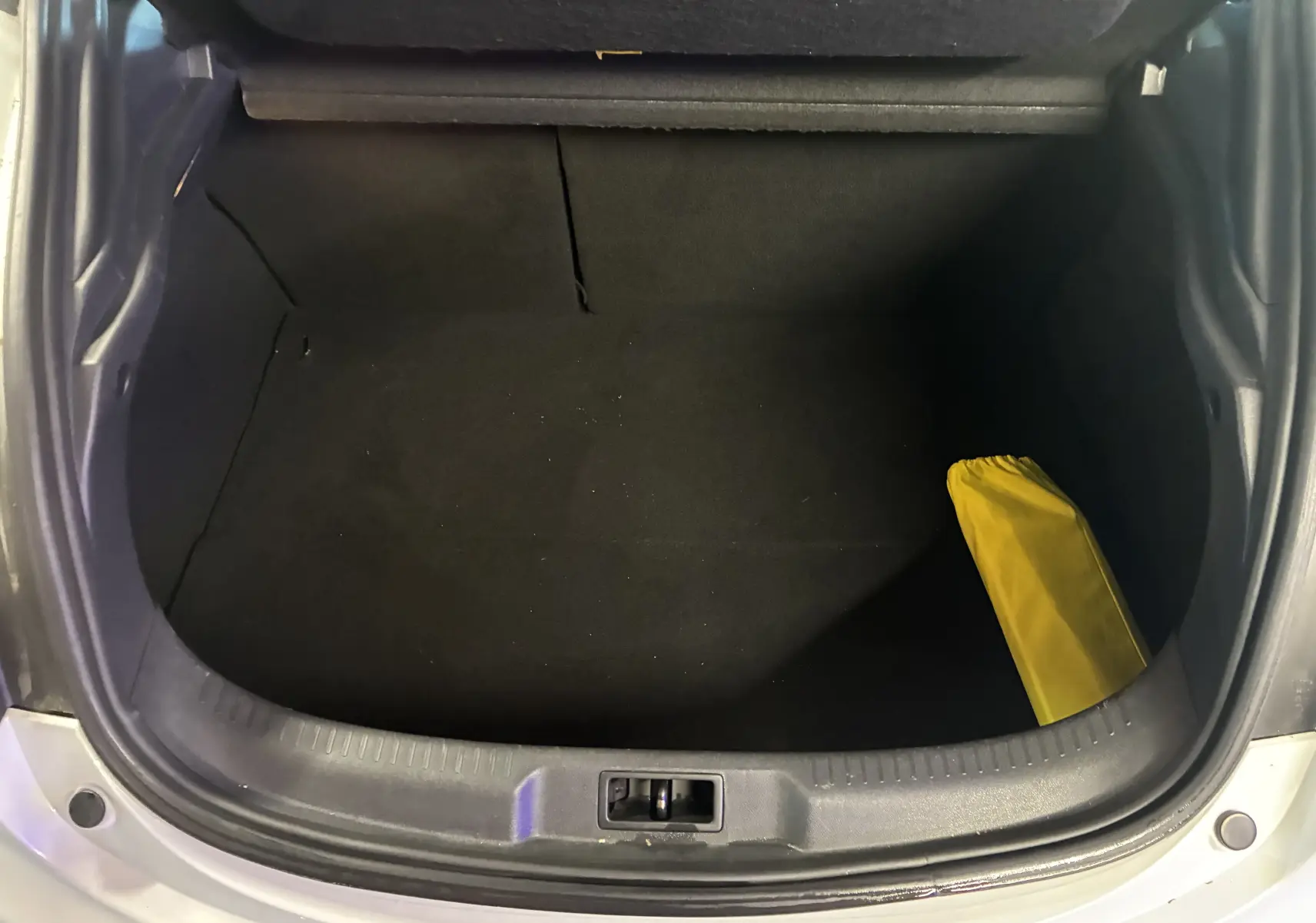 Coffre ouvert vu de dessus d'une Renault Mégane Coupé blanche, avec un objet jaune dans le coin droit.