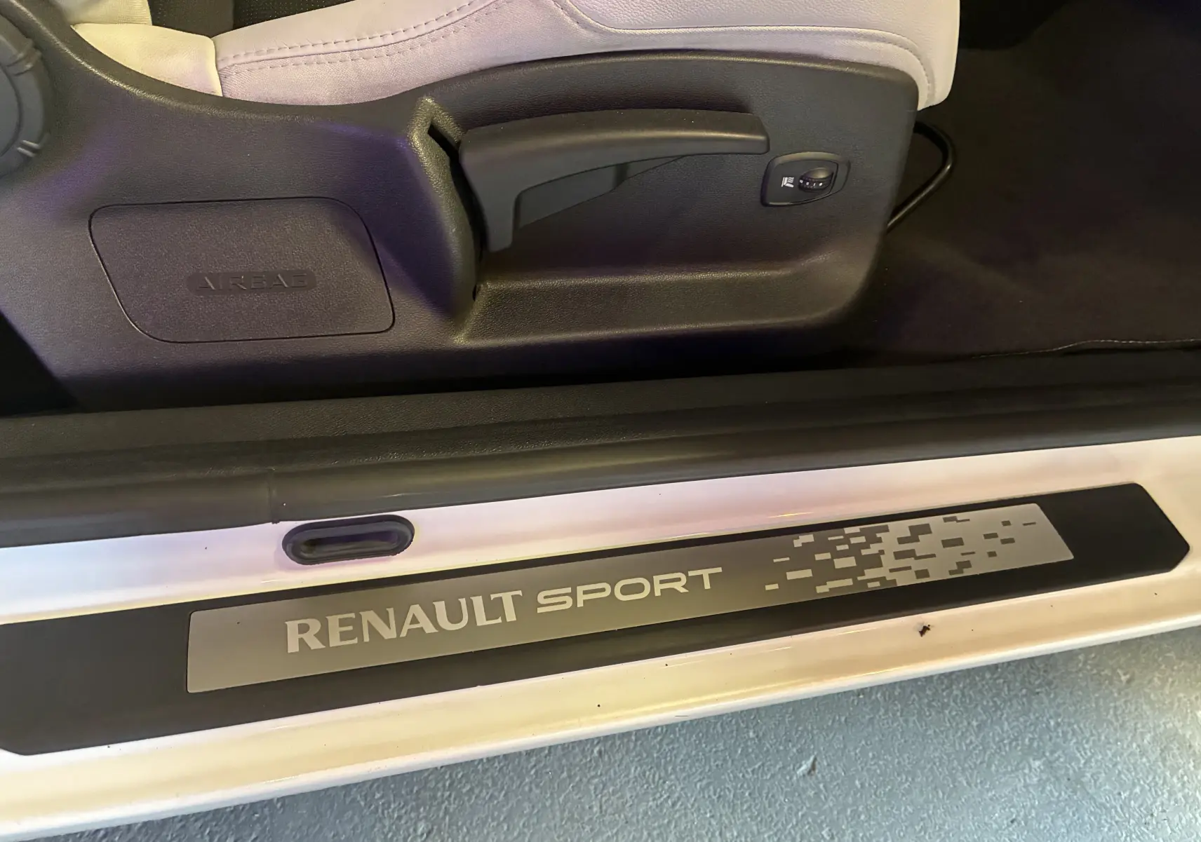 Détail de la marche intérieure blanche avec logo Renault Sport et réglage siège côté conducteur d’une Renault Mégane Coupé.