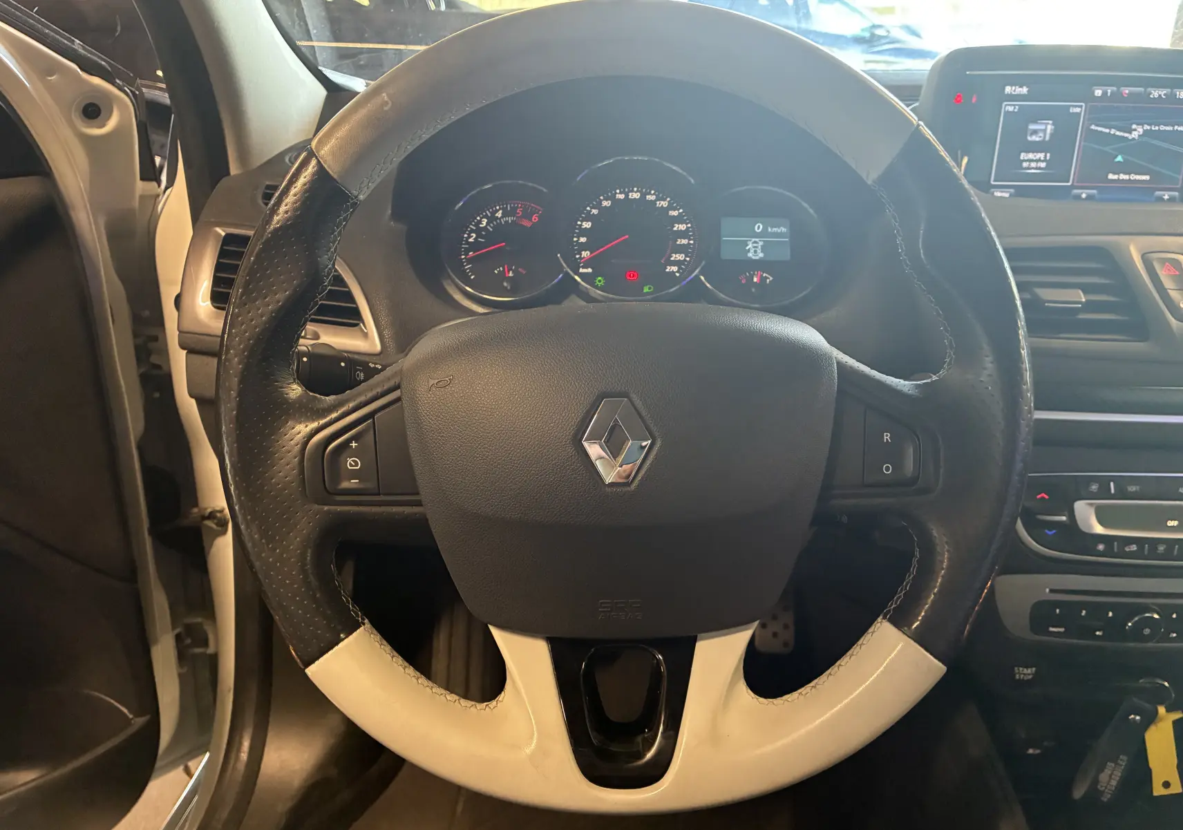 Vue rapprochée du volant cuir bicolore noir et blanc de la Renault Mégane Coupé 2.0 DCI 165 GT avec tableau de bord et écran tactile.