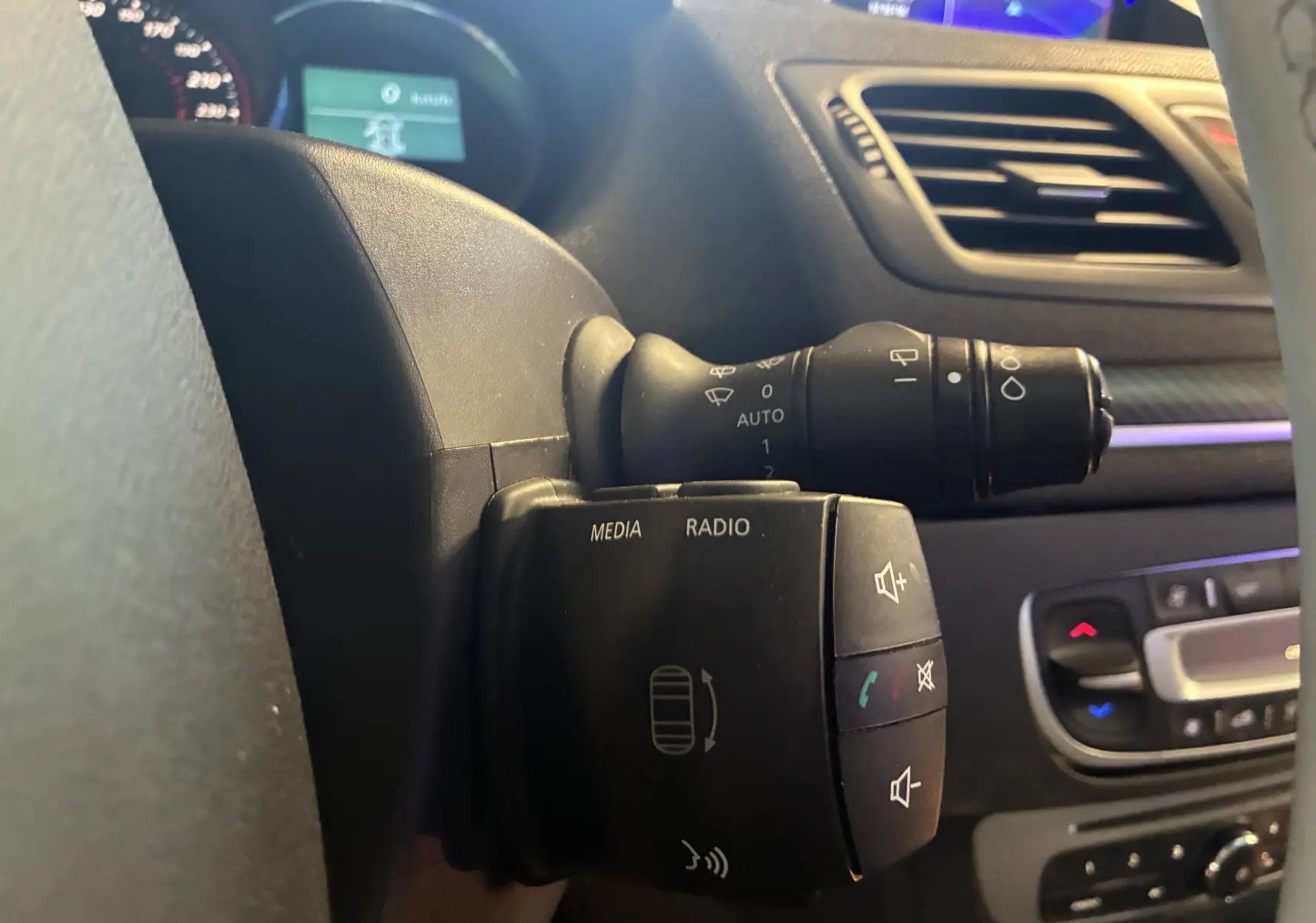 Gros plan sur la commande au volant côté gauche d’une Renault Mégane Coupé blanche, avec boutons média et radio visibles.