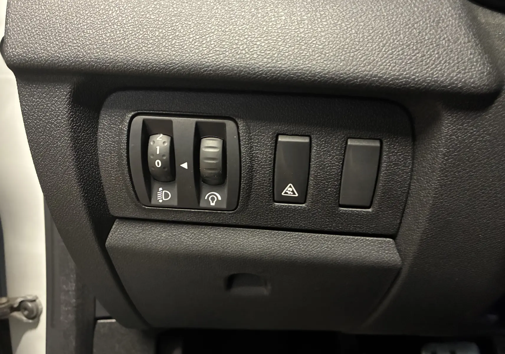 Gros plan sur les commandes de réglage des phares et du tableau de bord dans une Renault Mégane Coupé blanc 2014.