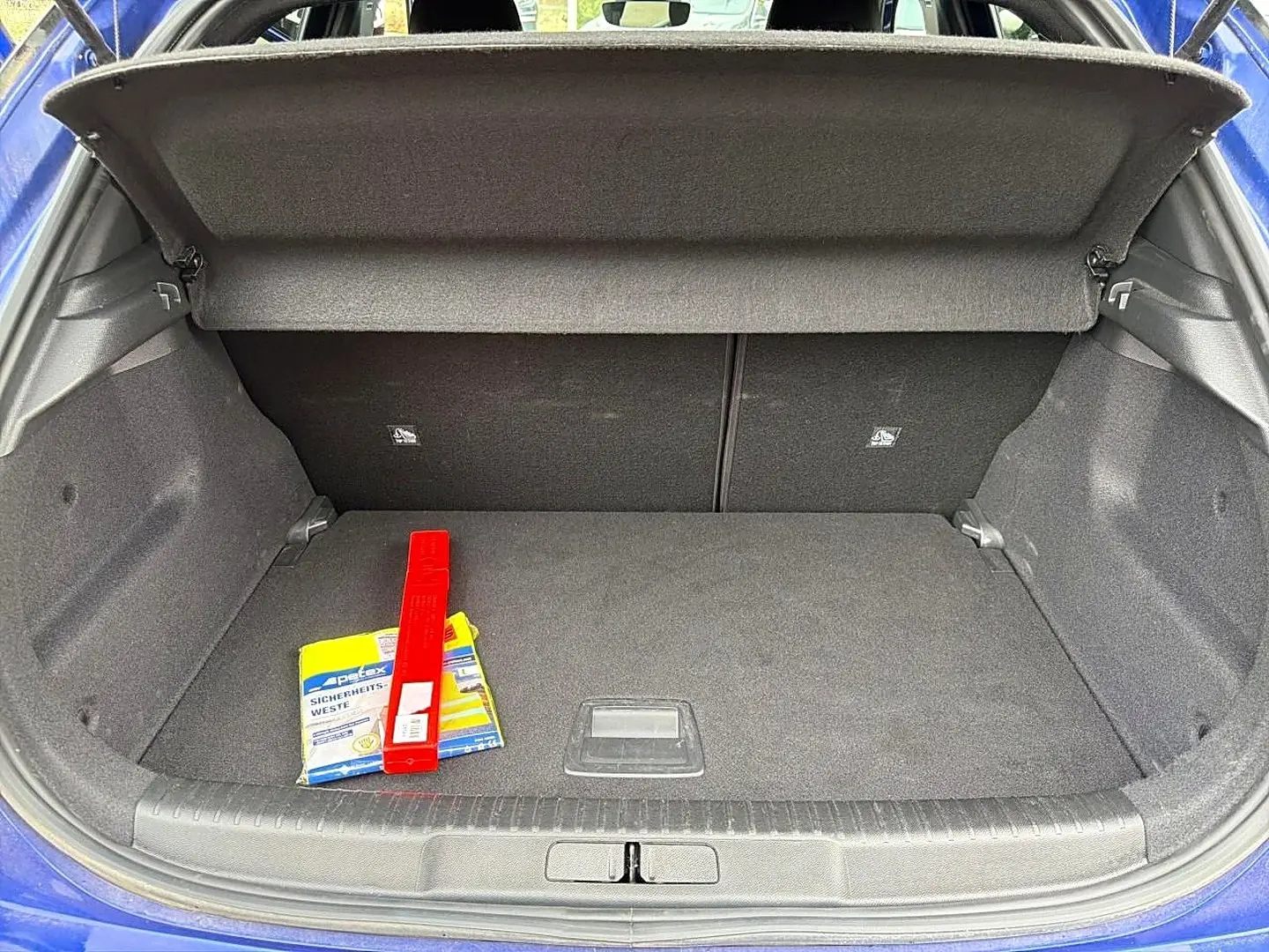 Vue du coffre ouvert d’un Opel Mokka bleu 2025, montrant un espace de rangement avec un triangle de signalisation et un gilet de sécurité.