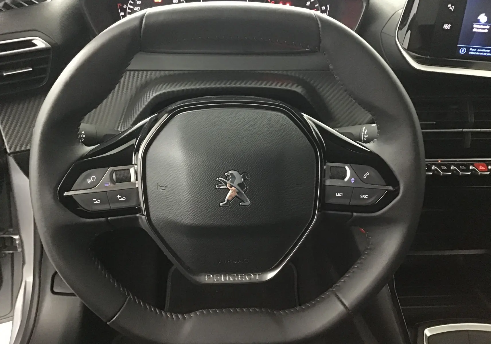 Gros plan sur le volant cuir noir du Peugeot 208 2022, avec commandes intégrées et tableau de bord en arrière-plan.