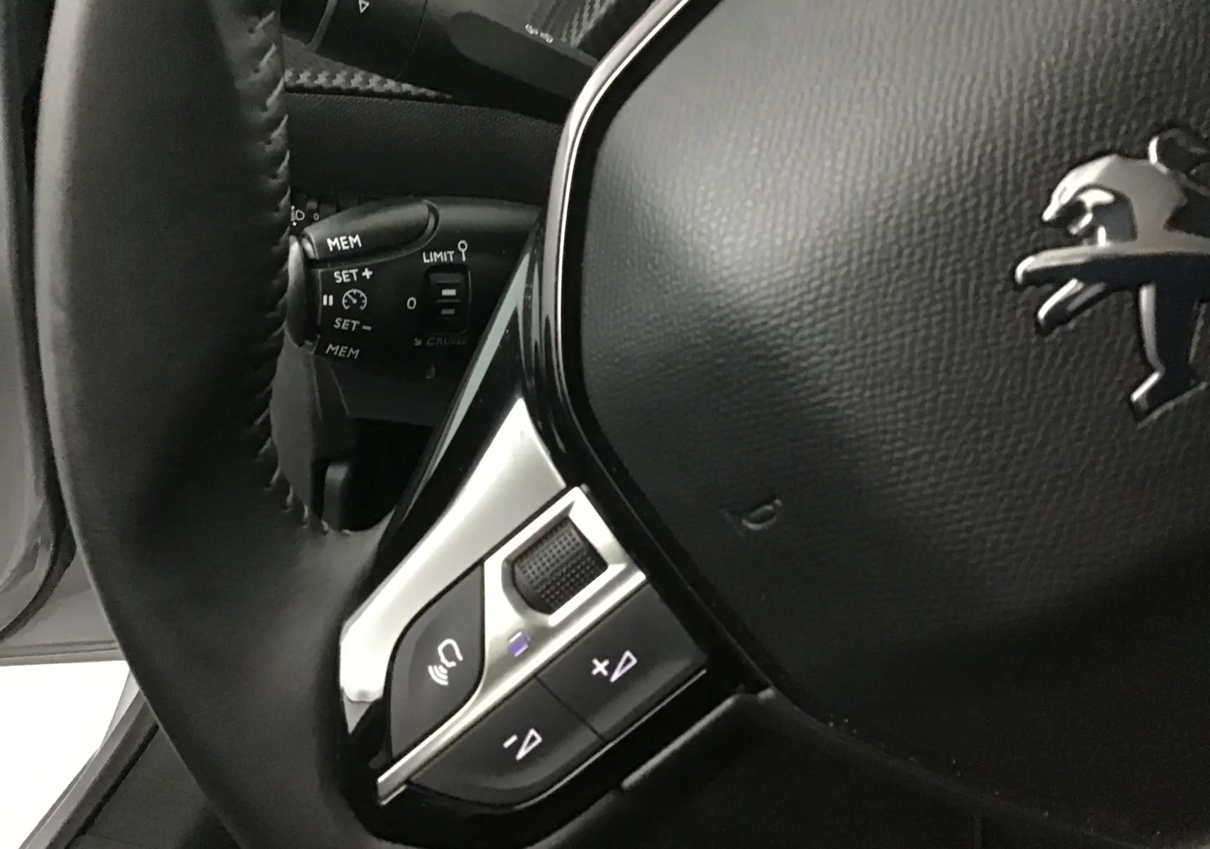 Gros plan sur le volant noir de la Peugeot 208 2022, mettant en valeur les commandes intégrées et le logo lion chromé.