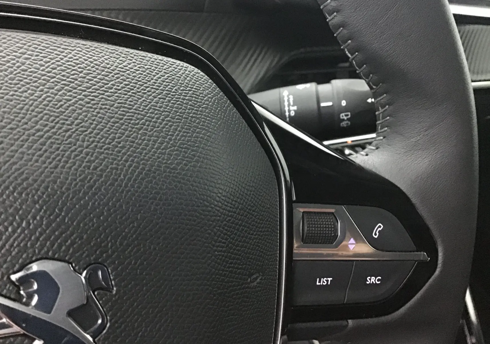 Gros plan sur le volant en cuir noir de la Peugeot 208 Gris Artense, avec commandes audio intégrées à droite.
