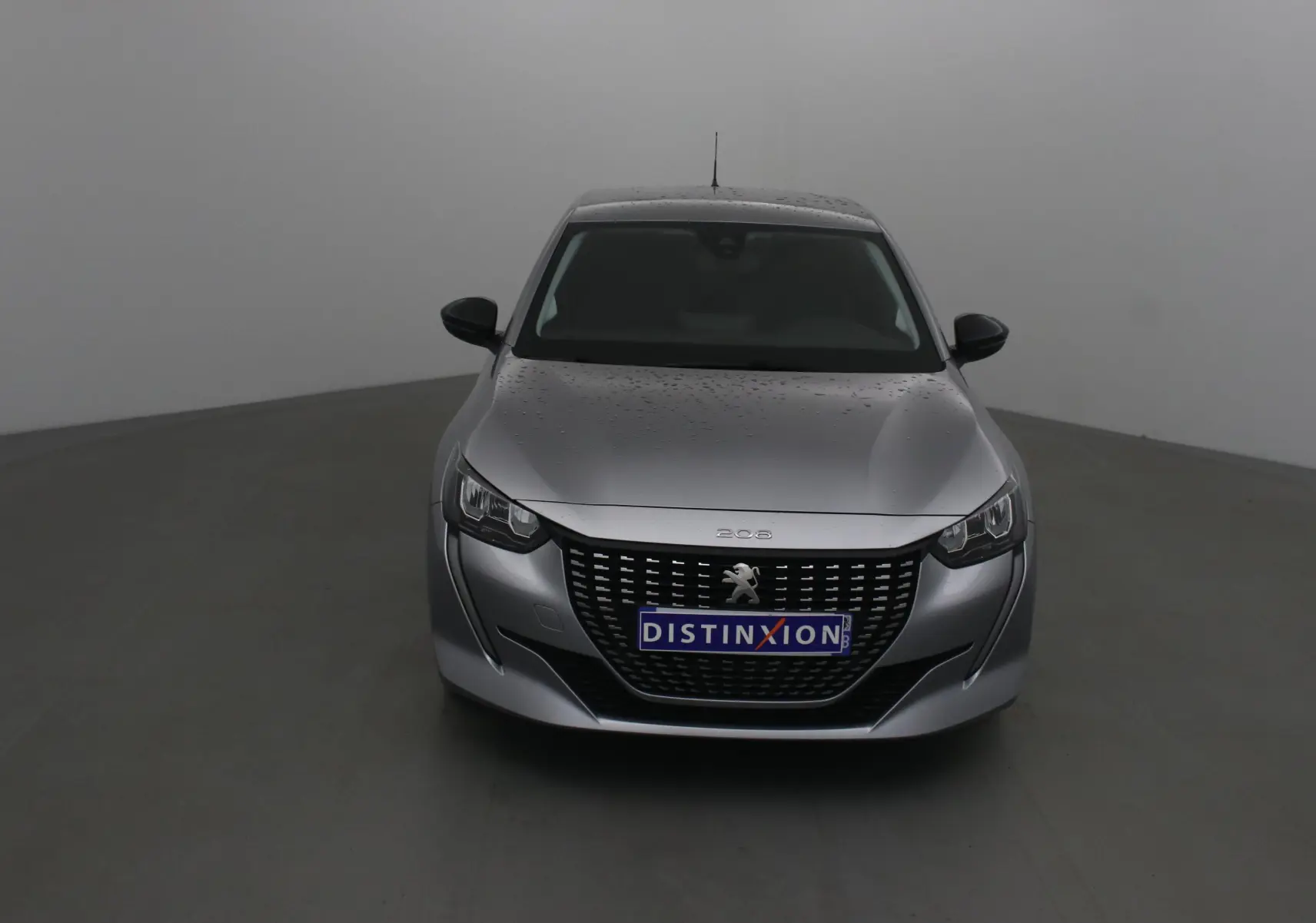 Peugeot 208 gris Artense vue de face avec calandre noire et logo lion distinctif sur fond neutre.