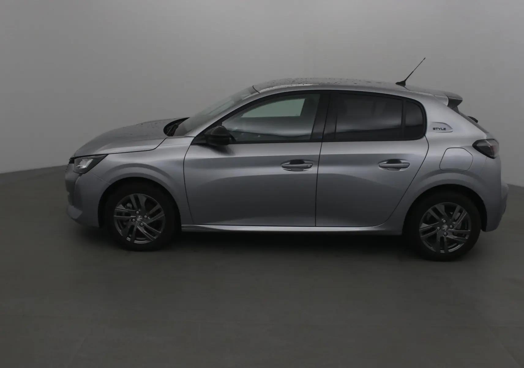 Profil côté gauche d'une Peugeot 208 gris Artense 2022 finition Style avec jantes alliage et vitres teintées.