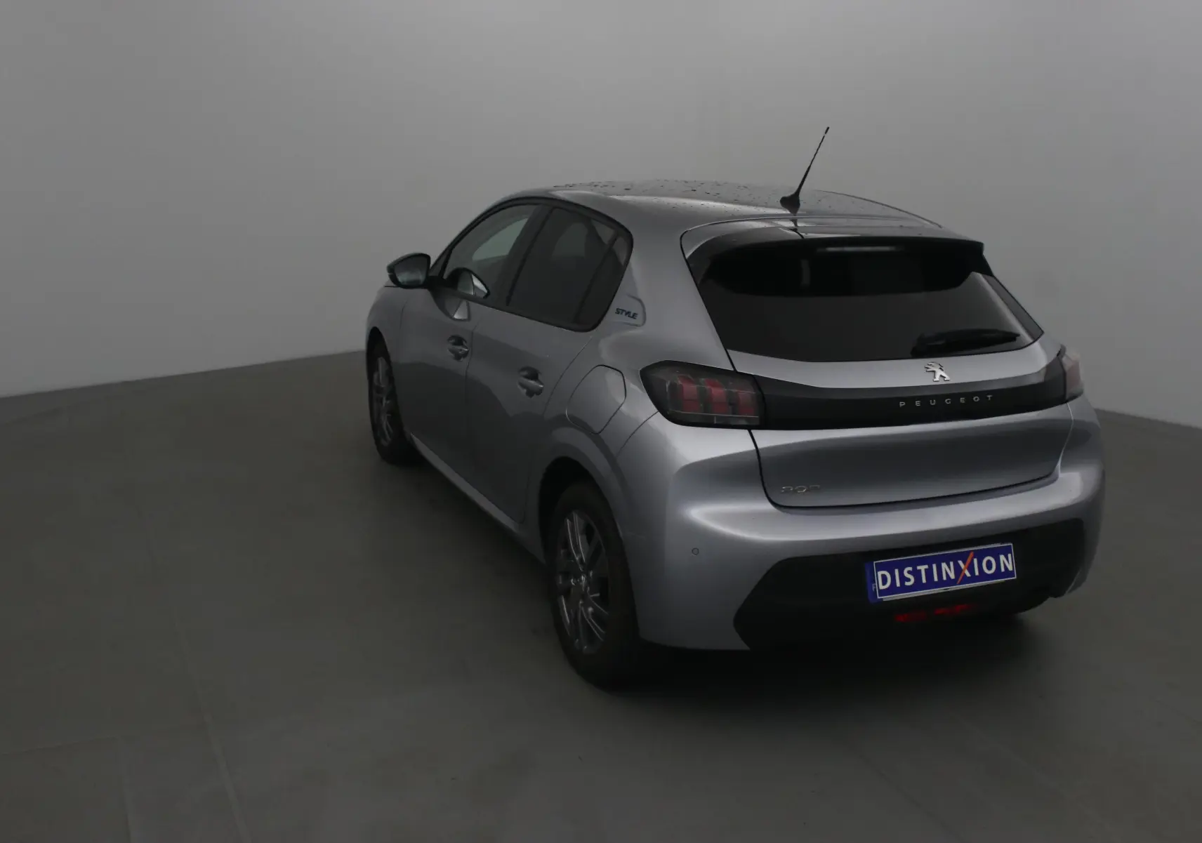 Peugeot 208 gris Artense vue 3/4 arrière côté gauche, avec logo Style sur l'aile arrière et vitres teintées.