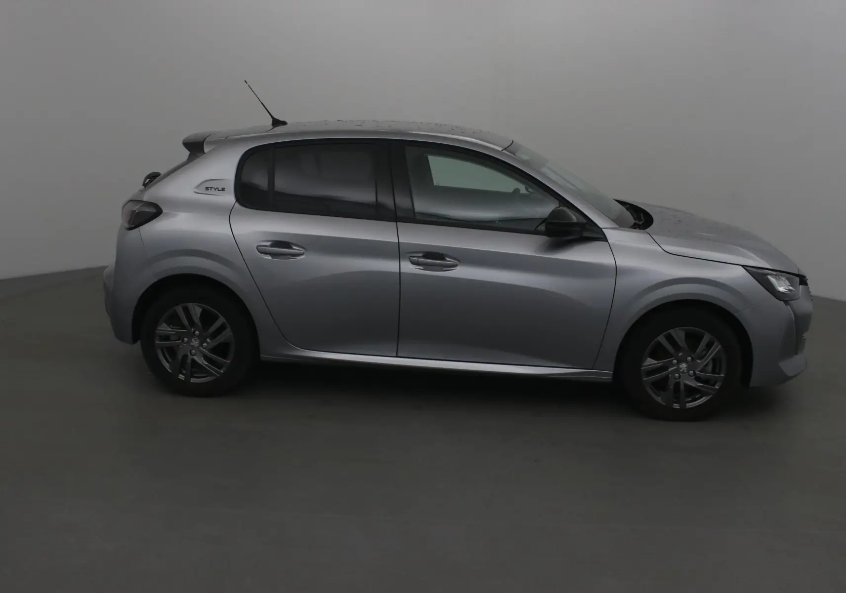 Profil droit d'une Peugeot 208 gris Artense 2022 version 1.2 PureTech 100 Style avec jantes alliage et vitres teintées.