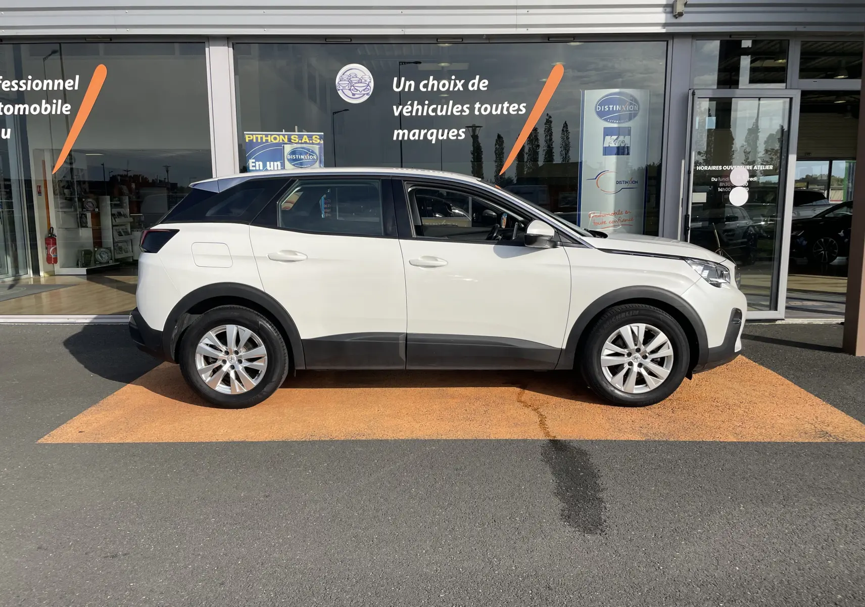 Profil droit d'un Peugeot 3008 blanc de 2018 garé devant une vitrine de concession automobile.