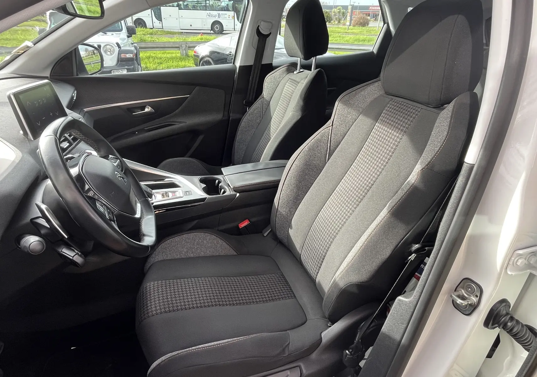 Vue intérieure côté conducteur du Peugeot 3008 blanc, mettant en valeur les sièges gris et noirs et le tableau de bord moderne.