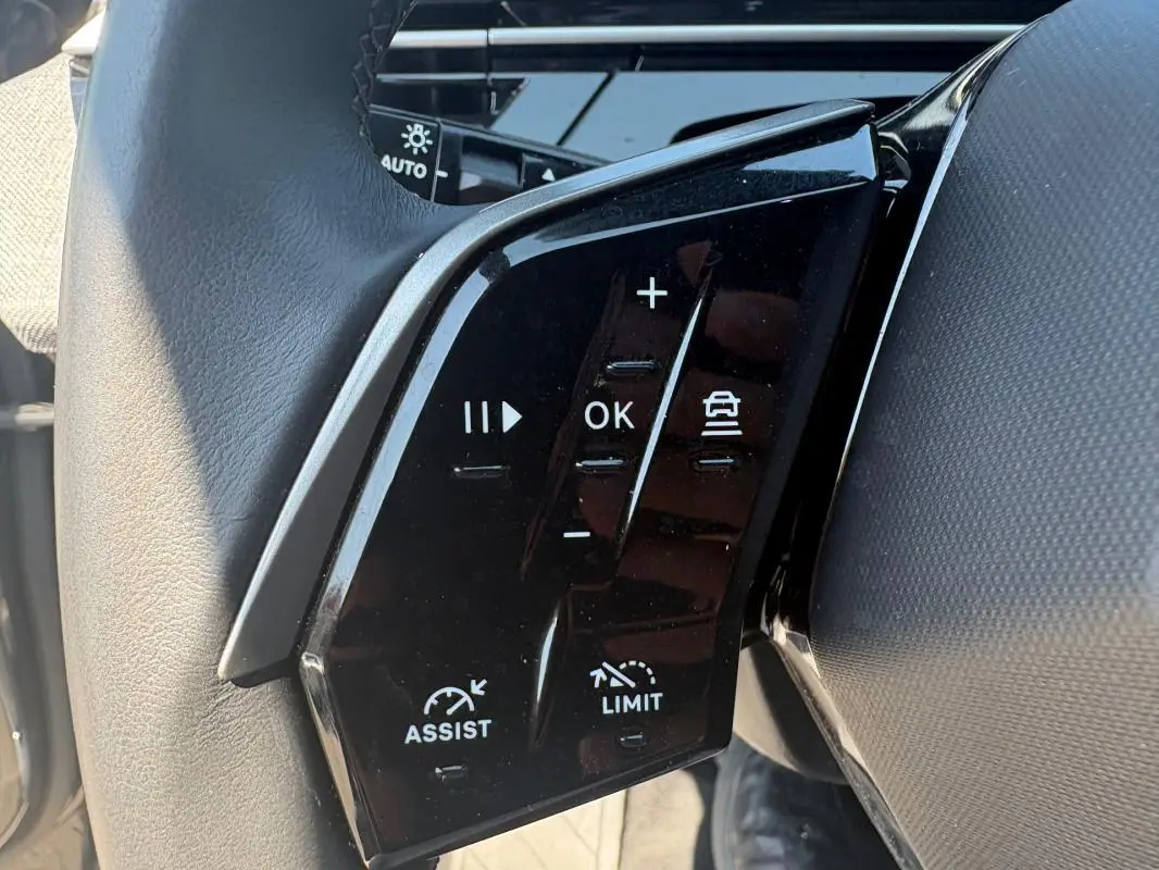 Gros plan sur les commandes au volant du Peugeot 3008 Hybrid 145 e-DCS6 Allure gris, montrant les boutons d'assistance et limiteur de vitesse.