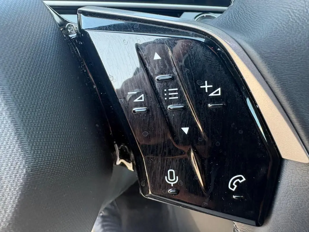 Gros plan sur les commandes au volant noir brillant du Peugeot 3008 Hybrid 145 e-DCS6 Allure gris, côté gauche.