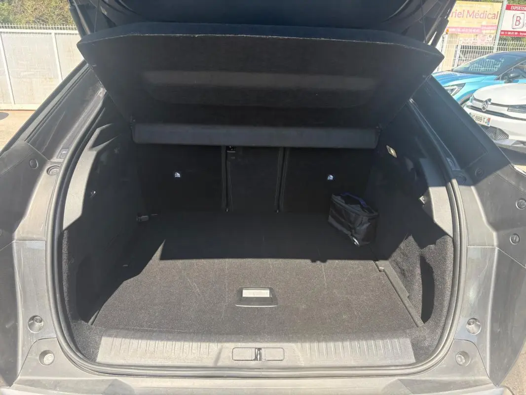 Coffre ouvert vu de l'arrière d'un Peugeot 3008 Hybrid gris, montrant un espace de chargement propre et spacieux.